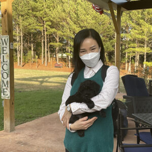 Masked woman holding mini Schnoodle puppy